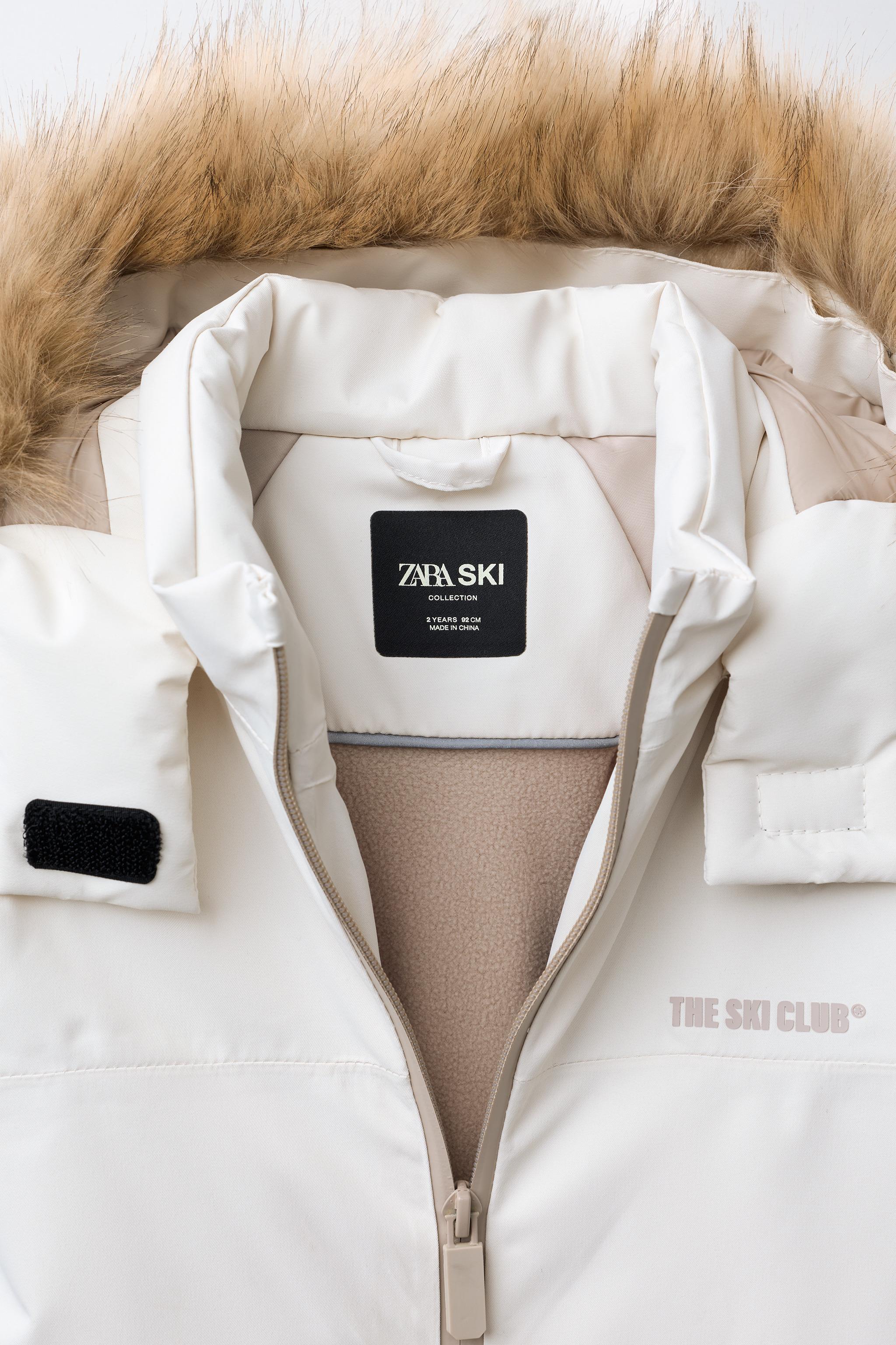 WATER RESISTANT AND WINDPROOF RECCO® SYSTEM SKI COLLECTION LONG JUMPSUIT WITH FAUX FUR HOODIE